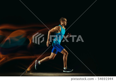 Professional male runner training isolated on black studio background in mixed light 54691944