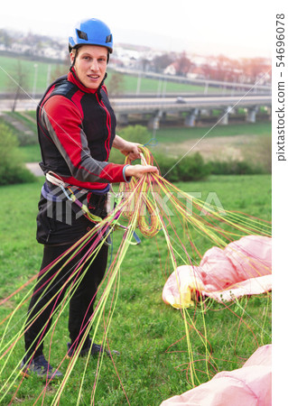 Landed young male paraglider raises parachute from 54696078