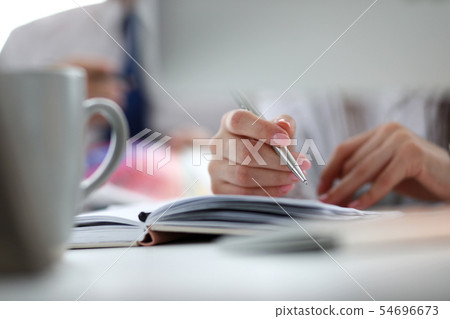 Hand of female executive holding silver pen making some creative memos Hand of female executive holding silver pen making some creative memos 54696673