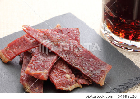 板岩板上的小吃，牛肉乾。在後面是一個可樂高的杯子。 54698126