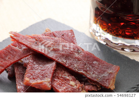 板岩板上的小吃，牛肉乾。在後面是一個可樂高的杯子。 54698127