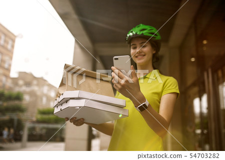 Young woman as a courier delivering pizza using gadgets Young woman as a courier delivering pizza using gadgets 54703282
