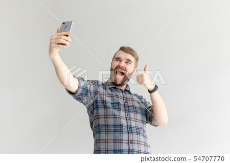 Side view of a positive funny handsome hipster guy and taking a selfie on a smartphone on white 54707770