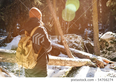 A bearded man in a hat and a backpack stands with his back on a sunny day in winter in a coniferous A bearded man in a hat and a backpack stands with his back on a sunny day in winter in a coniferous 54708274