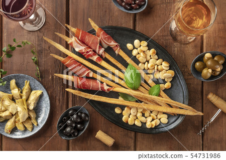 Italian antipasti. Grissini, parma, almonds, wine on a dark rustic wooden background Italian antipasti. Grissini, parma, almonds, wine on a dark rustic wooden background 54731986