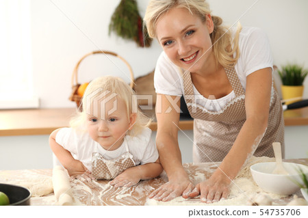 Little girl and her blonde mom in beige aprons playing and laughing while kneading the dough in Little girl and her blonde mom in beige aprons playing and laughing while kneading the dough in 54735706