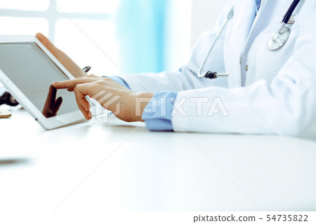 Doctor working table. Woman physician using tablet computer while sitting in hospital office close Doctor working table. Woman physician using tablet computer while sitting in hospital office close 54735822