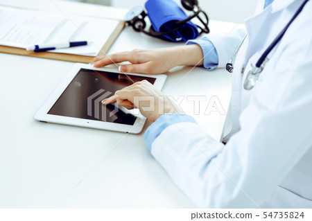 Doctor working table. Woman physician using tablet computer while sitting in hospital office close 54735824