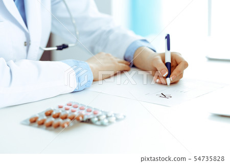 Female doctor filling up prescription form while sitting at the desk in hospital. Close-up of Female doctor filling up prescription form while sitting at the desk in hospital. Close-up of 54735828