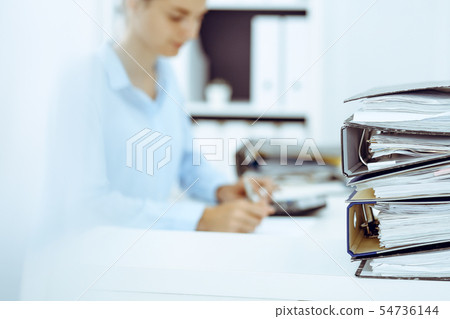 Binders with papers are waiting to be processed by business woman or bookkeeper back in blur Binders with papers are waiting to be processed by business woman or bookkeeper back in blur 54736144