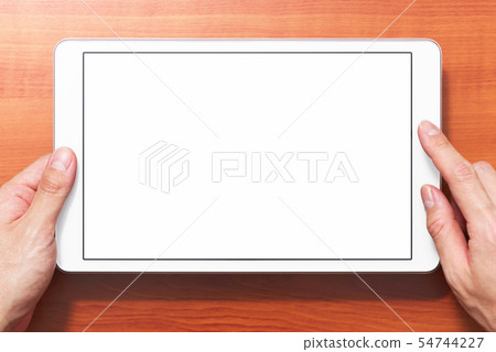 Close-up of a hand holding a white tablet PC seen from the front. Shadows on wood grain background. 54744227