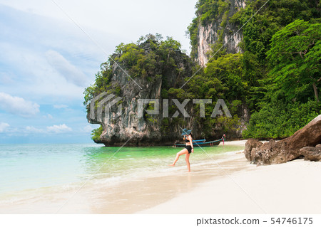 Happy woman in bikini and sunhat walking on sea beach. 54746175
