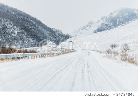 Empty mountain asphalt road in winter covered with snow on a cloudy day. The concept of driving a Empty mountain asphalt road in winter covered with snow on a cloudy day. The concept of driving a 54754845