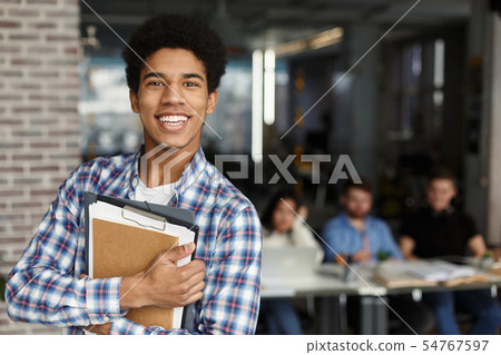 Happy student with books looking at camera in library Happy student with books looking at camera in library 54767597