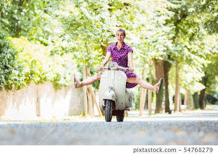 Carefree young woman driving scooter Carefree young woman driving scooter 54768279