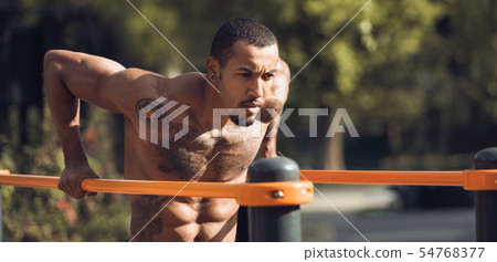 Muscular Guy Doing Street Workout, Exercising On Parallel Bars 54768377