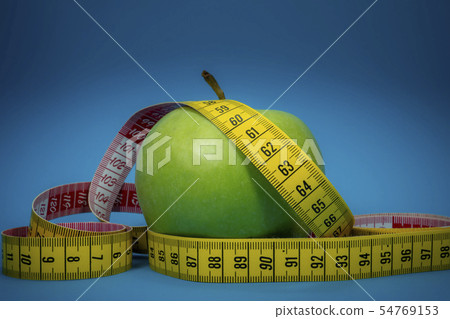 Measuring tape and green apple on blue background 54769153