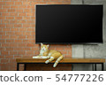 Cat sitting on wood table with Tv on brick wall 54777226