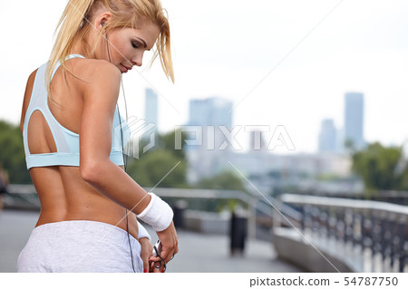 Beautiful woman during fitness on city is listen 54787750