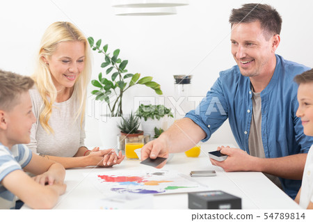 Happy young family playing card game at dining table at bright modern home. Happy young family playing card game at dining table at bright modern home. 54789814