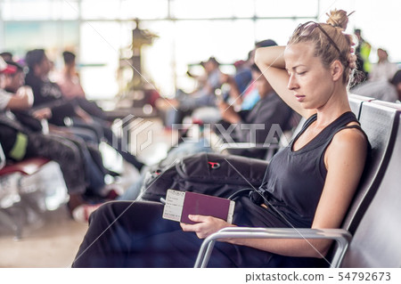 Casual tanned blond female traveler holding cell phone, passport and boarding pass while waiting to Casual tanned blond female traveler holding cell phone, passport and boarding pass while waiting to 54792673