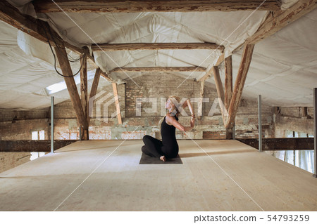 Young woman exercises yoga on an abandoned construction site Young woman exercises yoga on an abandoned construction site 54793259