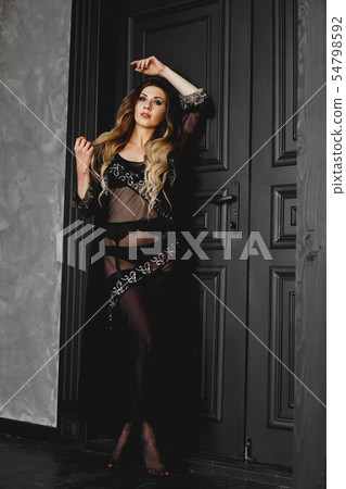 Young pretty woman, wearing transparent black peignoir night gown in dark room Young pretty woman, wearing transparent black peignoir night gown in dark room 54798592