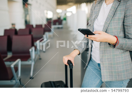 Girl at the airport with smartphone and baggage Girl at the airport with smartphone and baggage 54799793