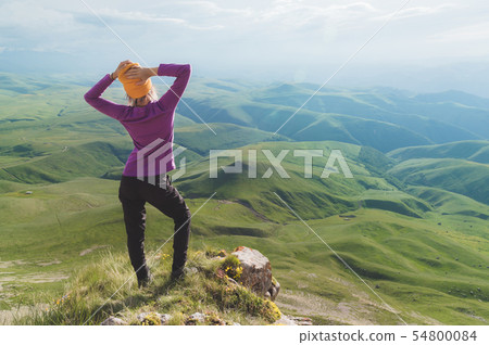 Rear view of an attractive female tourist standing on a grassy hill wearing sunglasses. Enjoying a 54800084