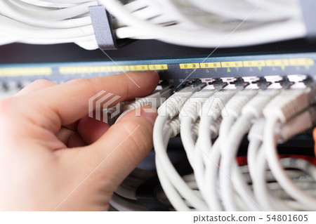 IT consultant connects a network cable into switch in large datacenter IT consultant connects a network cable into switch in large datacenter 54801605