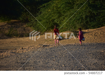 沙漠地區的Jaisalmer Coulee村莊在拉賈斯坦邦,印度運載井水的女孩在水瓶 沙漠地區的Jaisalmer Coulee村莊在拉賈斯坦邦,印度運載井水的女孩在水瓶 54807217