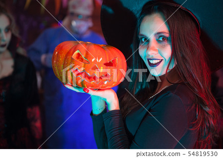 Close up portrait of beautiful woman dressed up like a witch for halloween holding a pumpkin Close up portrait of beautiful woman dressed up like a witch for halloween holding a pumpkin 54819530