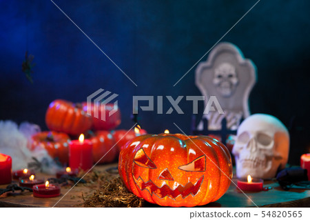 Halloween pumpkin glowing in front of a creepy skull on a wooden table 54820565