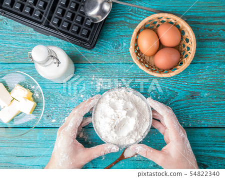Making waffles at home - waffle iron, batter in bowl and ingredients - milk, eggs and flour. 54822340