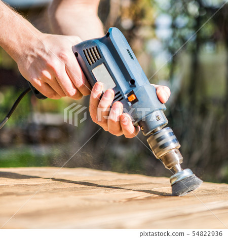 Hands man with electrical rotating brush metal disk sanding a piece of wood Hands man with electrical rotating brush metal disk sanding a piece of wood 54822936