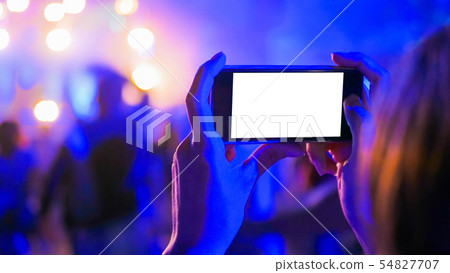 Woman hand silhouette holding smartphone with white empty display at concert 54827707