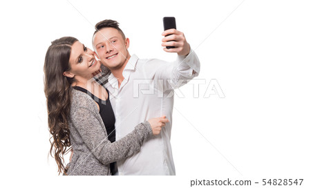 Selfie time. Beautiful young couple hugging and smiling while making selfie, standing over white 54828547