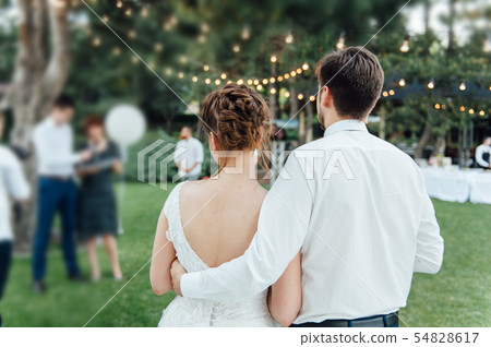 Look from behind on guests sitting on white chairs during the ceremony Look from behind on guests sitting on white chairs during the ceremony 54828617