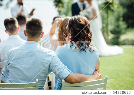 Look from behind on guests sitting on white chairs during the ceremony 54828653