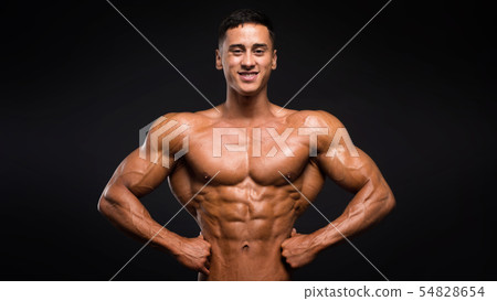 Smiley sportsman showing his muscles over dark background. 54828654