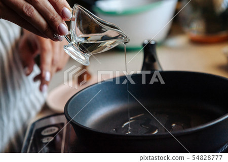Vegetable oil pouring from a bottle into a frying pan. 54828777
