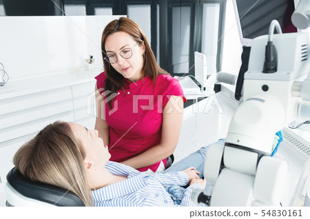 Dentist woman doctor talking to a young patient sitting on the dentist chair in a medical office Dentist woman doctor talking to a young patient sitting on the dentist chair in a medical office 54830161