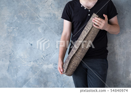 Closeup male hand holding yoga mat over bright gray background, copy space. 54840974