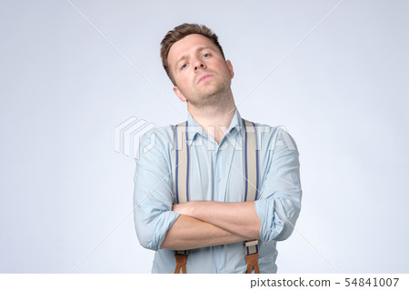 Serious selfish man with folded arms and suspenders posing at studio. Serious selfish man with folded arms and suspenders posing at studio. 54841007