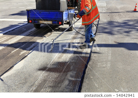 Worker repairs part of the asphalt road, spraying 54842941