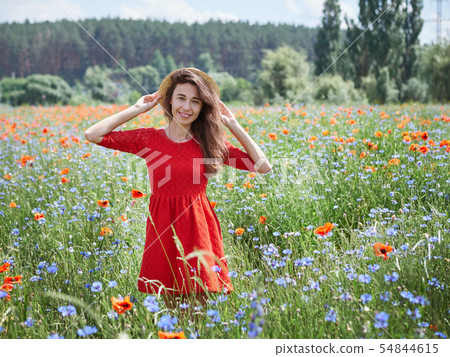 Lovely young romantic woman in straw hat on poppy flower field posing on background summer. Wearing 54844615