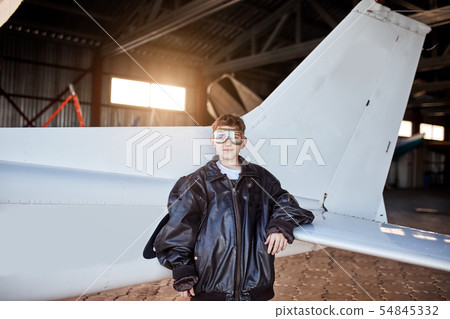 portrait of little boy standing besides light white airplane tail inside aircraft shed portrait of little boy standing besides light white airplane tail inside aircraft shed 54845332