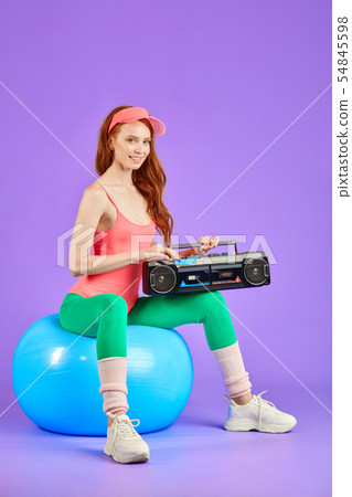 studio shot of female model poising at camera for retro style photoshoot with portable cassette studio shot of female model poising at camera for retro style photoshoot with portable cassette 54845598