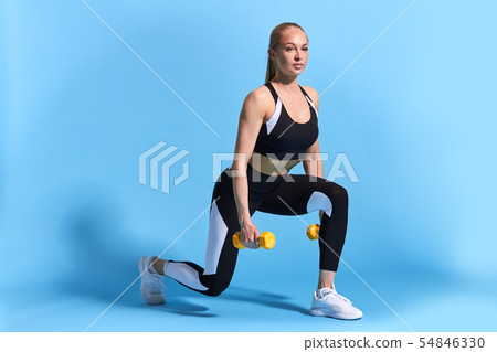 Beautiful young slim fit woman doing lunge exercise with yellow dumbbells Beautiful young slim fit woman doing lunge exercise with yellow dumbbells 54846330