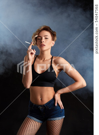 arrogant blonde model in top , shorts, fishnet holding a cigarette 54847568